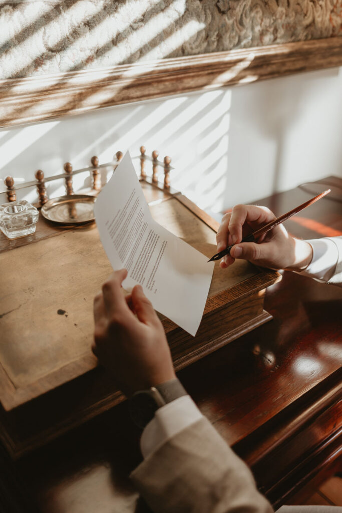 Groom writing vows on a vintage desk with an old pen