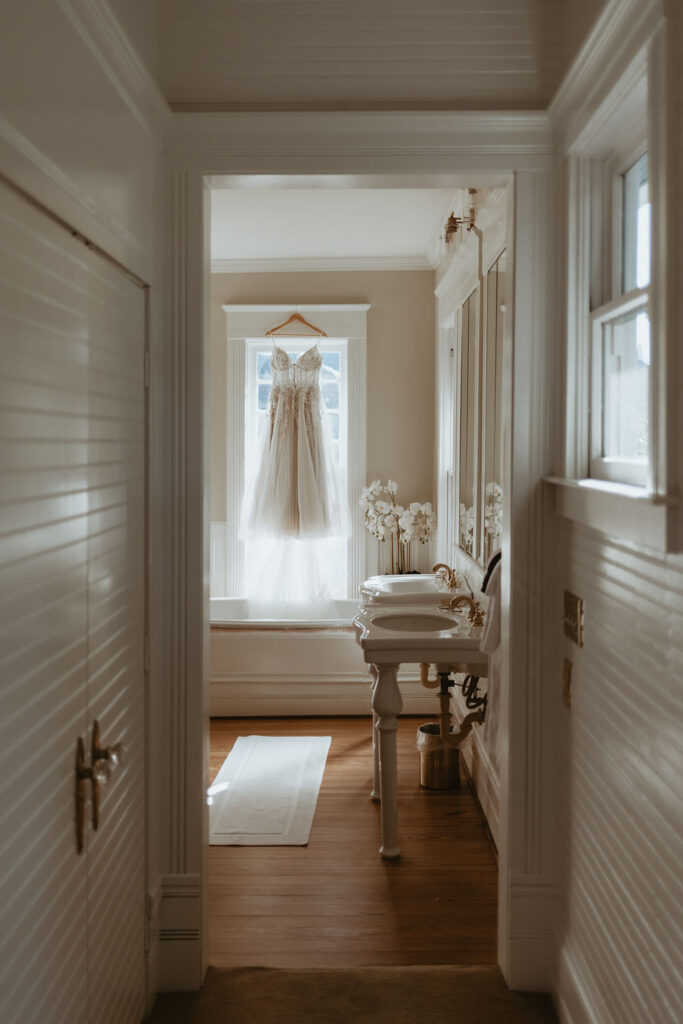 Brides dress hanging in the window of a vintage style bathroom