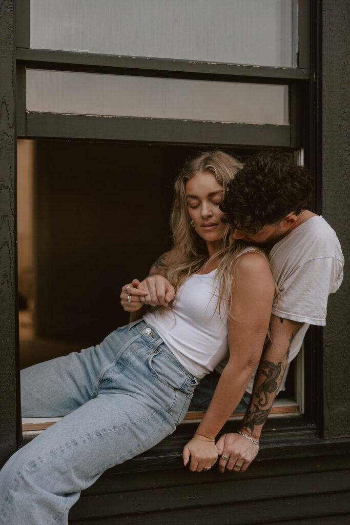 Couple sit in a window sill like sneaky teenagers