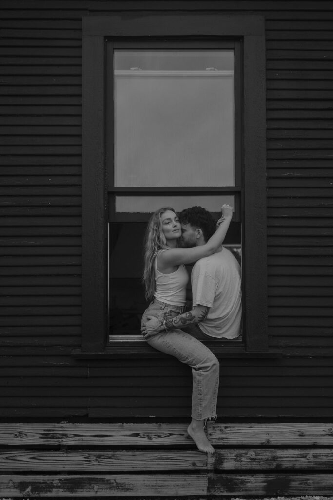 Couple sit in a window sill like sneaky teenagers