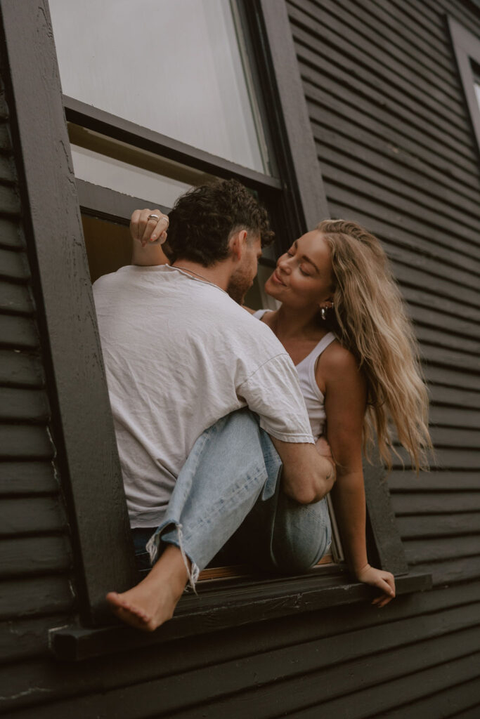 Couple sit in a window sill like sneaky teenagers