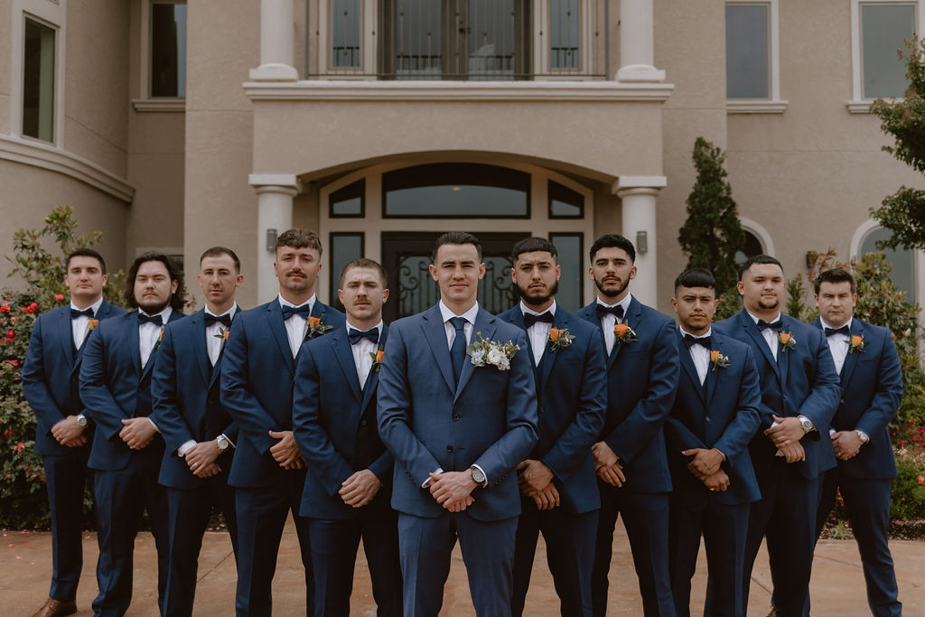 Groom and groomsmen stand in front of the Texas wedding venue