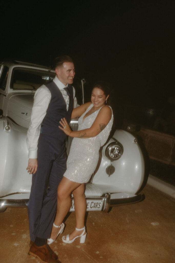 Bride and groom lean on a vintage car