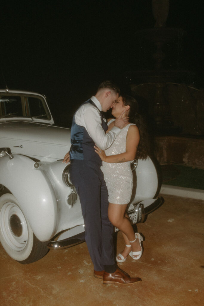 Bride and groom lean on a vintage car