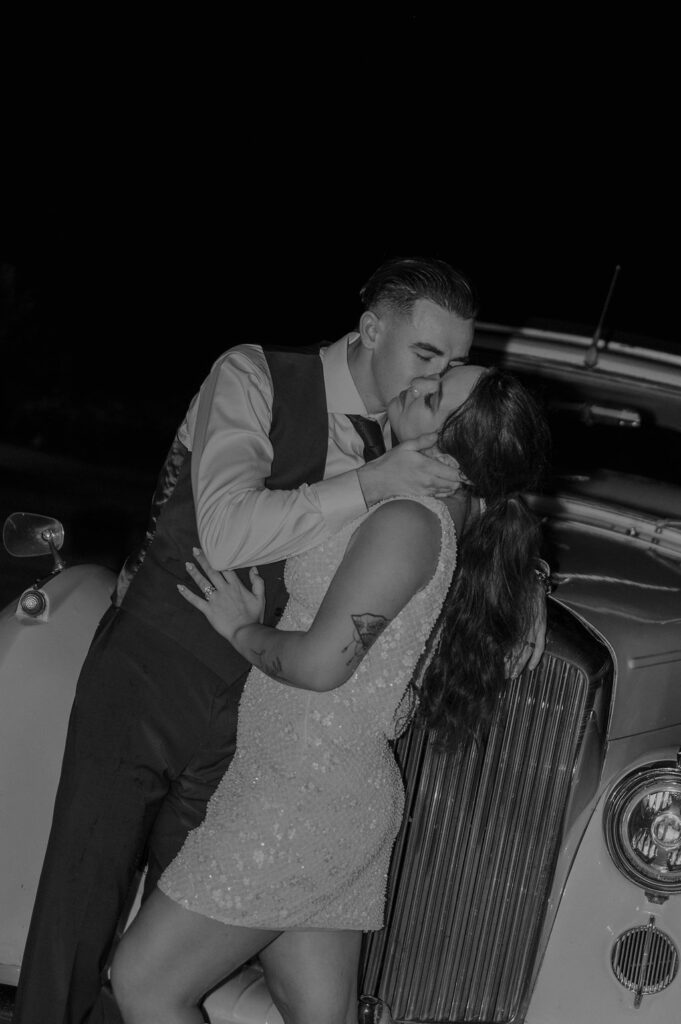 Bride and groom lean on a vintage car