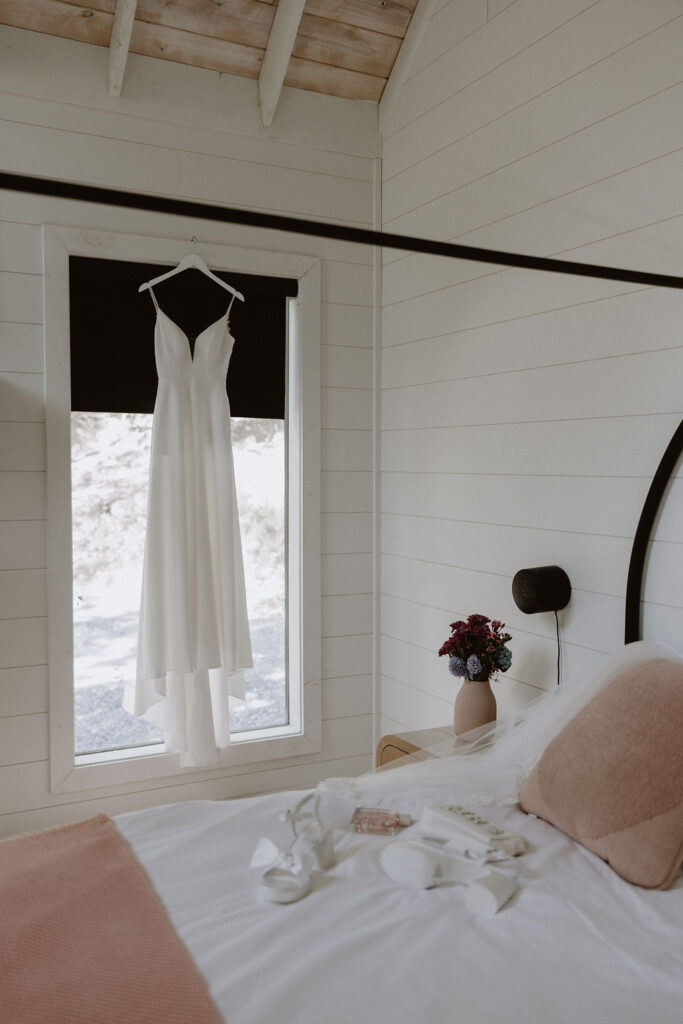 Brides simple white wedding dress hangs in the window of their Airbnb