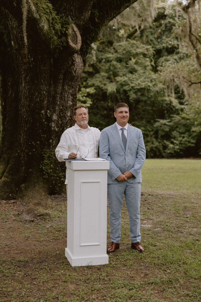 Groom stands with the officiant during the elopement ceremony as he watches his bride walk down the aisle