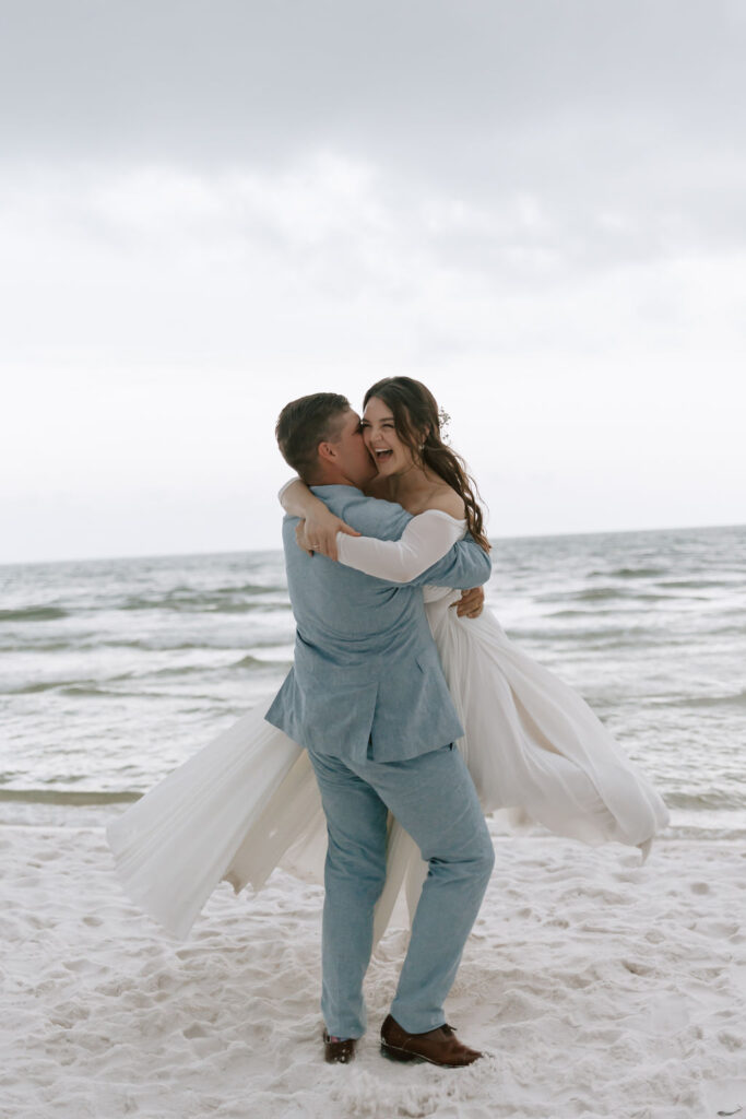 Playfully swings bride around on the white sandy beach in Destin, Florida