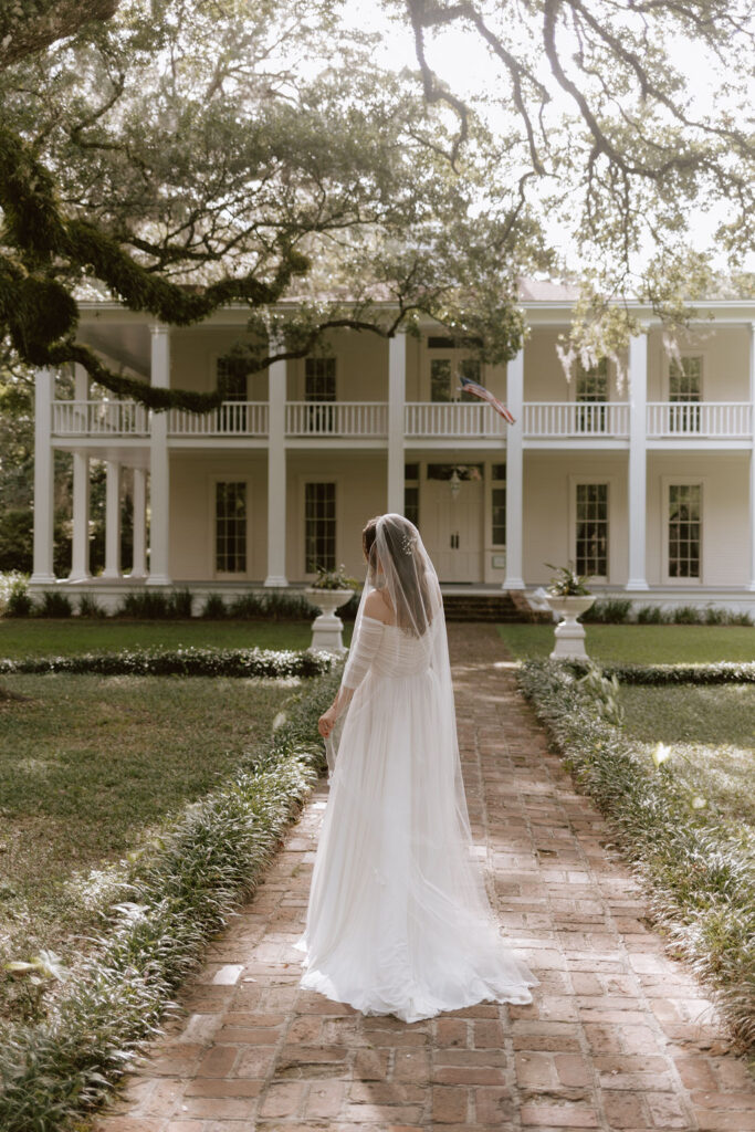 Bride poses in front of a beautiful old white home in Eden Garden State Park