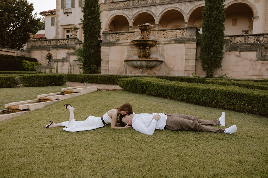 A couple playfully lays on the lawn in front of Philbrook Museum of art