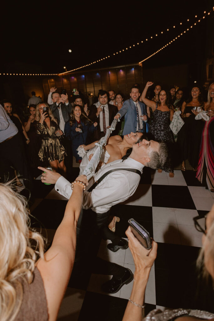 Bride and groom do the limbo with their guests on the dance floor using napkins as the bar