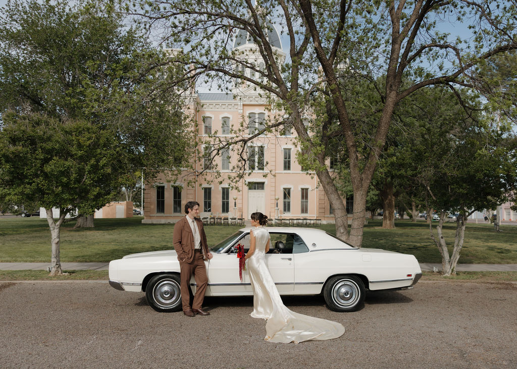 Bride and groom posing with old car in front of Marfa Courthouse