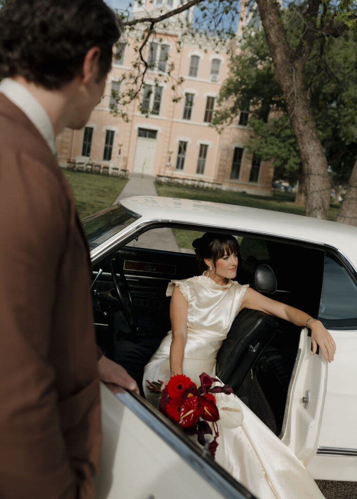 Bride and groom posing with old car in front of Marfa Courthouse